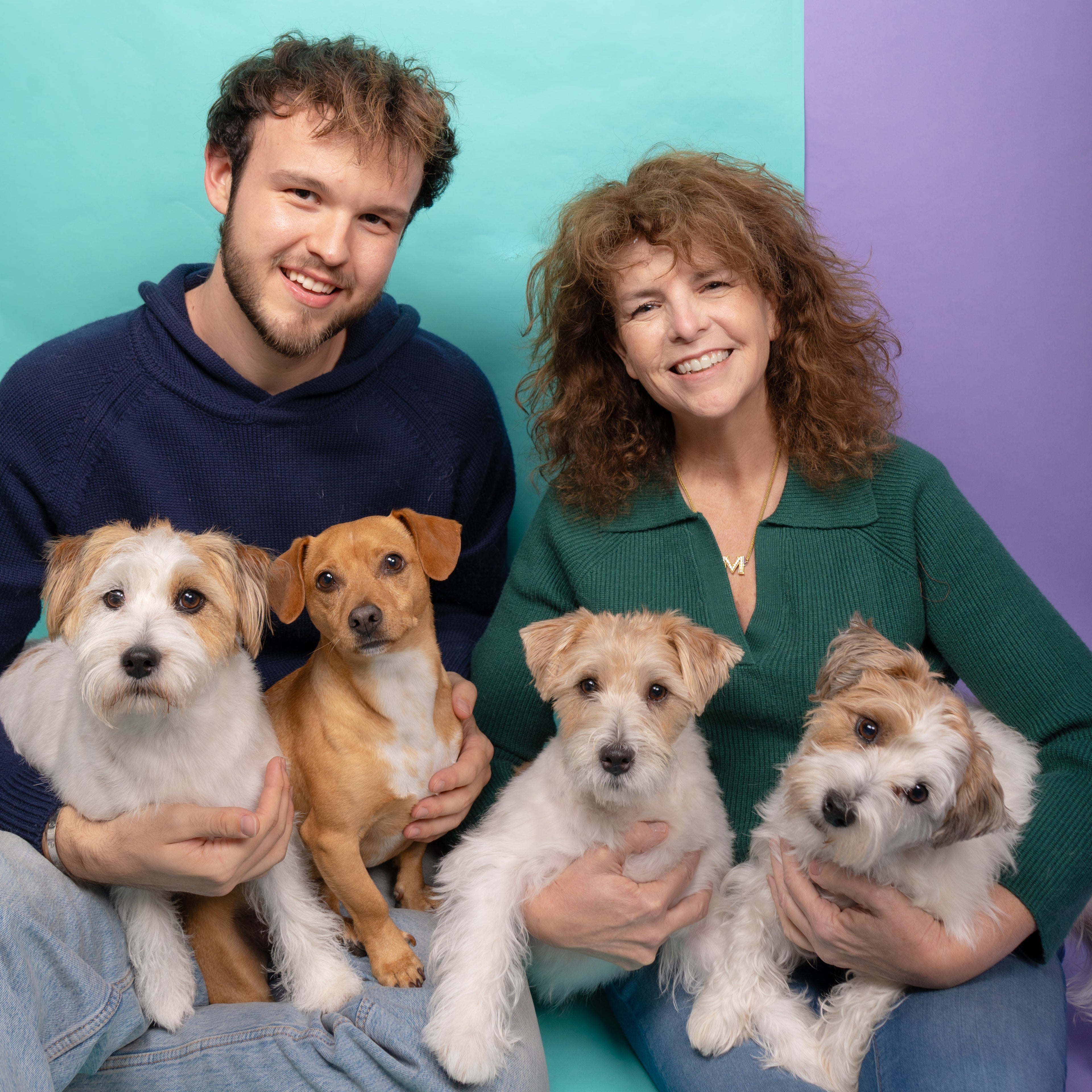 Two people holding four dogs against a colorful background